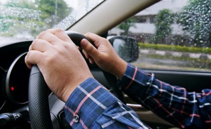 Image: Adobe. A pair of hands on a car steering wheel.